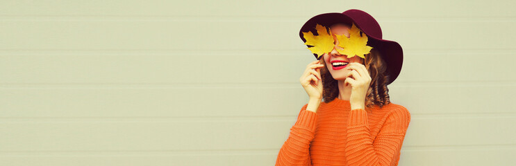 autumn portrait of happy surprised smiling woman covering her eyes with yellow maple leaves wearing 