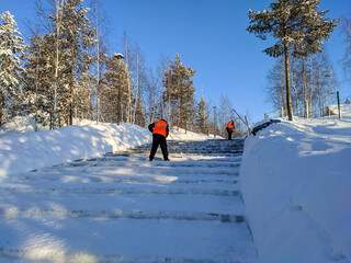 Noyabrsk, Russia - February 5, 2022: People in bright overalls clean the stairs in the park from snow with a shovel