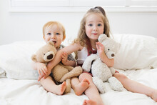 Portrait Of Brother (12-17 Months) And Sister (2-3) Sitting On Bed With Teddy Bears