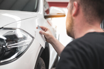 a man holding a palette with a color sample near a modern car, compares car paint with the color palette and makes a choice.