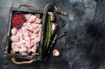 Wall Mural - Raw Diced chicken breast fillets, sliced poultry meat in wooden tray. Black background. Top view. Copy space