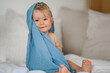 mega cute naked almost one year old blond baby boy sitting & laughing at home on a cozy bed after bathing and playing with a blue muslin fabric burp cloth while making nonsense jokes