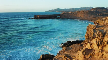 Wall Mural - Rocky coastline alongside cliff, blue Atlantic Ocean water reflect at sunset. Nature landscape. Golden sandstone bluff beach. Amazing aerial view. Travel destination. Fuerteventura Island, Canaries.