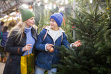 Fototapeta  - Happy mother with teenager daughter choose christmas tree at street fair