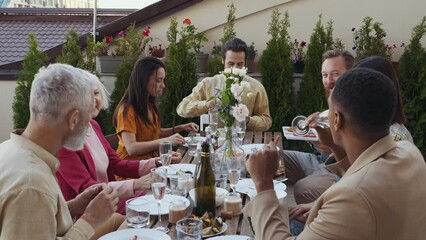 Wall Mural - Family and friends celebrating at dinner on a rooftop terrace. Multiethnic group of people dining on the balcony on a special evening to celebrate friendship and family love and relationships