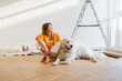 Young woman sits with her dog in room while making repairment in apartment. Repair and house renovation concept, friendship with pet