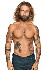 Handsome man with beard and long hair standing shirtless showing tattoos looking sleepy and tired, exhausted for fatigue and hangover, lazy eyes in the morning.