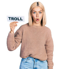 Canvas Print - Beautiful young blonde woman holding troll banner scared and amazed with open mouth for surprise, disbelief face