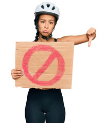 Sticker - Beautiful hispanic woman wearing bike helmet and holding stop banner with angry face, negative sign showing dislike with thumbs down, rejection concept