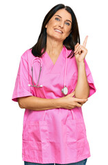 Poster - Middle age brunette woman wearing doctor uniform and stethoscope smiling happy pointing with hand and finger to the side