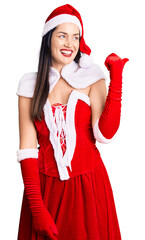 Poster - Young beautiful caucasian woman wearing santa claus costume smiling with happy face looking and pointing to the side with thumb up.