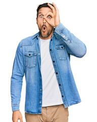 Wall Mural - Young handsome man wearing casual denim jacket doing ok gesture shocked with surprised face, eye looking through fingers. unbelieving expression.