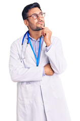 Wall Mural - Young hispanic man wearing doctor uniform and stethoscope with hand on chin thinking about question, pensive expression. smiling and thoughtful face. doubt concept.