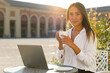 © Paulista - Young student or businesswoman enjoy a cup of cappuccino and look at camera while sitting in an outdoor cafe with her laptop.