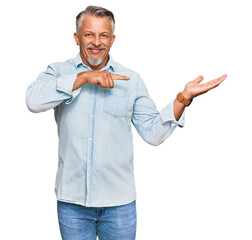 Sticker - Middle age grey-haired man wearing casual clothes amazed and smiling to the camera while presenting with hand and pointing with finger.