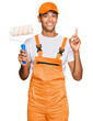© Krakenimages.com - Young handsome african american man wearing cap and painter clothes holding painting roll surprised with an idea or question pointing finger with happy face, number one