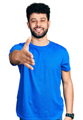 Sticker - Young arab man with beard wearing casual blue t shirt smiling cheerful offering palm hand giving assistance and acceptance.