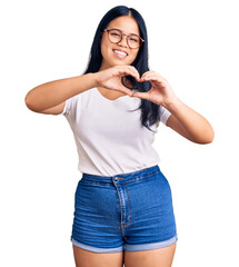 Young beautiful asian girl wearing casual clothes and glasses smiling in love doing heart symbol shape with hands. romantic concept.