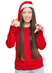 Poster - Young chinese woman wearing christmas hat smiling funny doing claw gesture as cat, aggressive and sexy expression