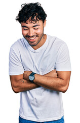 Wall Mural - Hispanic young man with beard wearing casual white t shirt smiling and laughing hard out loud because funny crazy joke with hands on body.