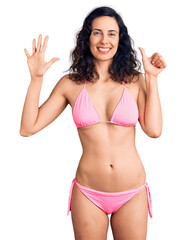 Wall Mural - Young beautiful hispanic woman wearing bikini showing and pointing up with fingers number six while smiling confident and happy.