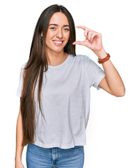 Sticker - Young hispanic girl wearing casual white t shirt smiling and confident gesturing with hand doing small size sign with fingers looking and the camera. measure concept.