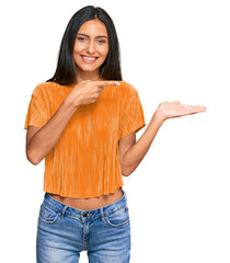 Poster - Young brunette arab woman wearing casual clothes amazed and smiling to the camera while presenting with hand and pointing with finger.