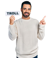 Poster - Young hispanic man with beard holding troll banner smiling happy pointing with hand and finger to the side