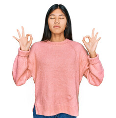 Wall Mural - Beautiful young asian woman wearing casual winter sweater relax and smiling with eyes closed doing meditation gesture with fingers. yoga concept.