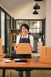 © Prathankarnpap - Young woman entrepreneur working in home office, preparing parcel boxes of product for delivery. Online selling, e-commerce concept