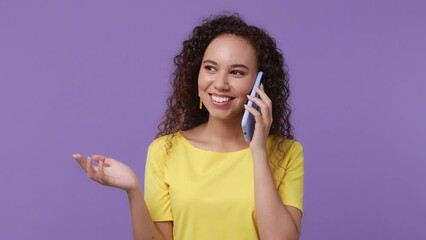 Wall Mural - Young happy smiling calm woman of African American ethnicity 20s she wear yellow t-shirt hold use talk on mobile cell phone conducting pleasant conversation isolated on plain pastel purple background