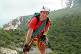 Fototapeta  - Climber climbs the mountain on a cable with a view of the forest and the sea.