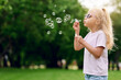 © khmelev - Cheerful caucasian blond preschool girl wearing sunglasses blowing soap bubbles in summer park outdoors and have fun. Happy childhood concept