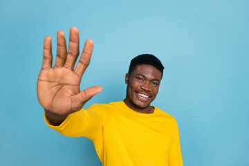 Wall Mural - Photo of diversity funny guy raise arm towards you say hey see old friend wear yellow long sleeve shirt isolated blue color background