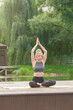 © Natasha  - A woman sitting on a wooden platform by a pond in summer, does yoga