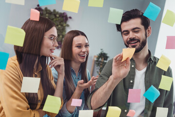 Wall Mural - Photo of three cheerful business people discuss new project start-up ideas making notes analyzing company strategy in office