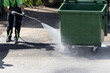 A municipal service worker treats a garbage container with a disinfectant solution. Washing the garbage container.