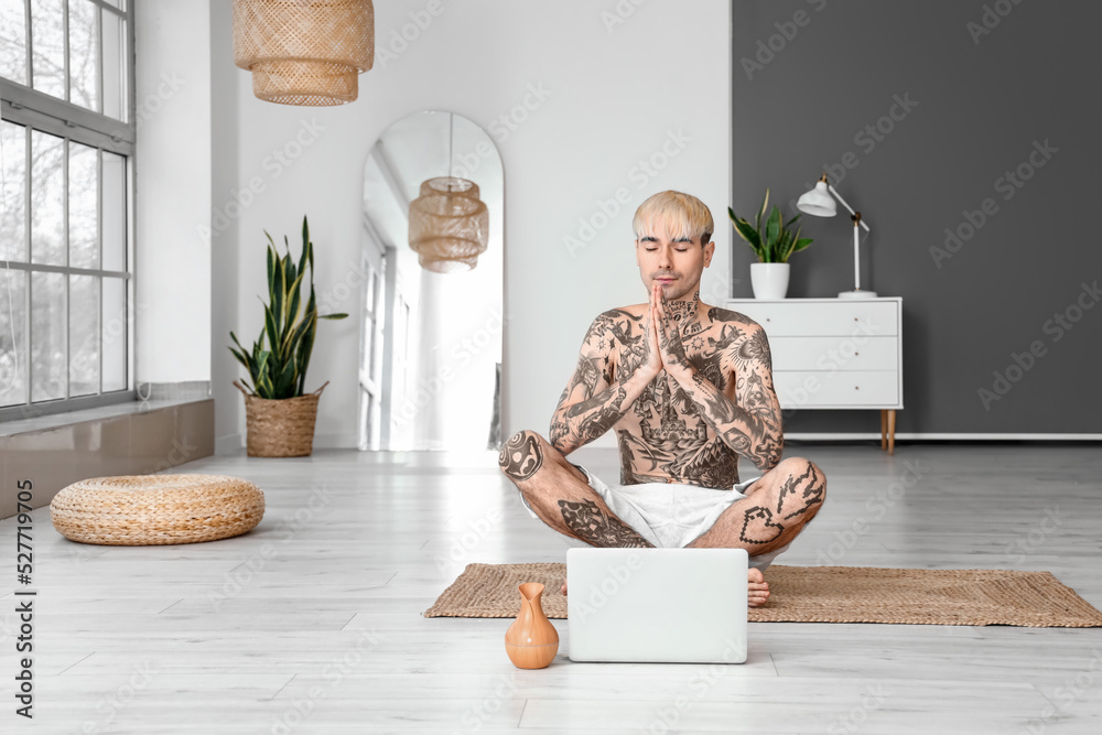 Young tattooed man meditating at home