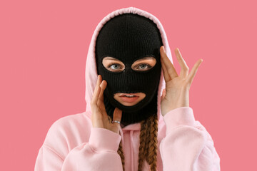 Wall Mural - Portrait of young woman in balaclava touching face on pink background