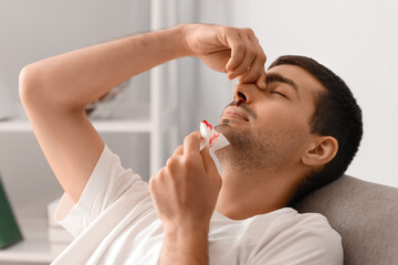 Young man with nosebleed holding tissue at home, closeup