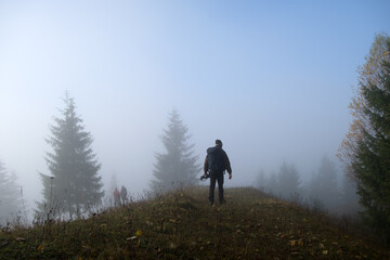 Small figure of lonely hiker enjoying his time on wild forest trail on foggy autumn day