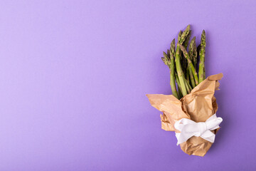 Wall Mural - Overhead view of copy space by asparagus bunch tied in paper with ribbon on purple background