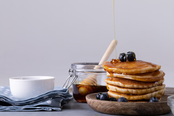 Close-up of stacked pancakes with blue berries and dripping honey against gray background