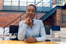 Portrait Of Confident African American Young Businesswoman With Hand On Chin At Desk In Office