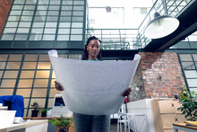 African American Young Female Architect Holding Blueprint While Standing In Modern Office