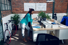 African American Young Female Architect Using Smart Phone While Working At Desk In Modern Office