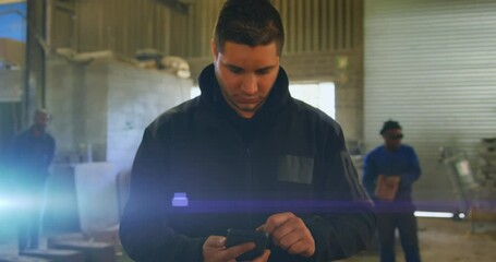 Poster - Animation of glowing light over caucasian man using smartphone working in factory