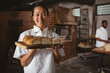 © Wavebreak Media - Portrait of smiling asian mid adult female baker holding serving board with fresh breads
