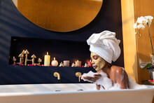 African American Woman Blowing Soap Sud On Hand While Relaxing In Bath Tub At Home