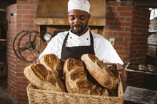 African American Mid Adult Male Baker Holding Breads In Wicker Basket While Standing In Bakery